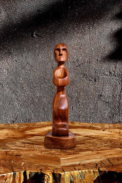 Live Edge Sculpture Iroko Prayer. The "Iroko Prayer" Live Edge sculpture is a captivating wooden statue and work of art that will add a touch of elegance to your home. Crafted from the richly-grained Iroko wood, revered for its healing properties, this striking sculpture features a beautifully hand-carved wooden figurine mounted on a sleek black walnut raw edge plinth. Original wood sculpture.